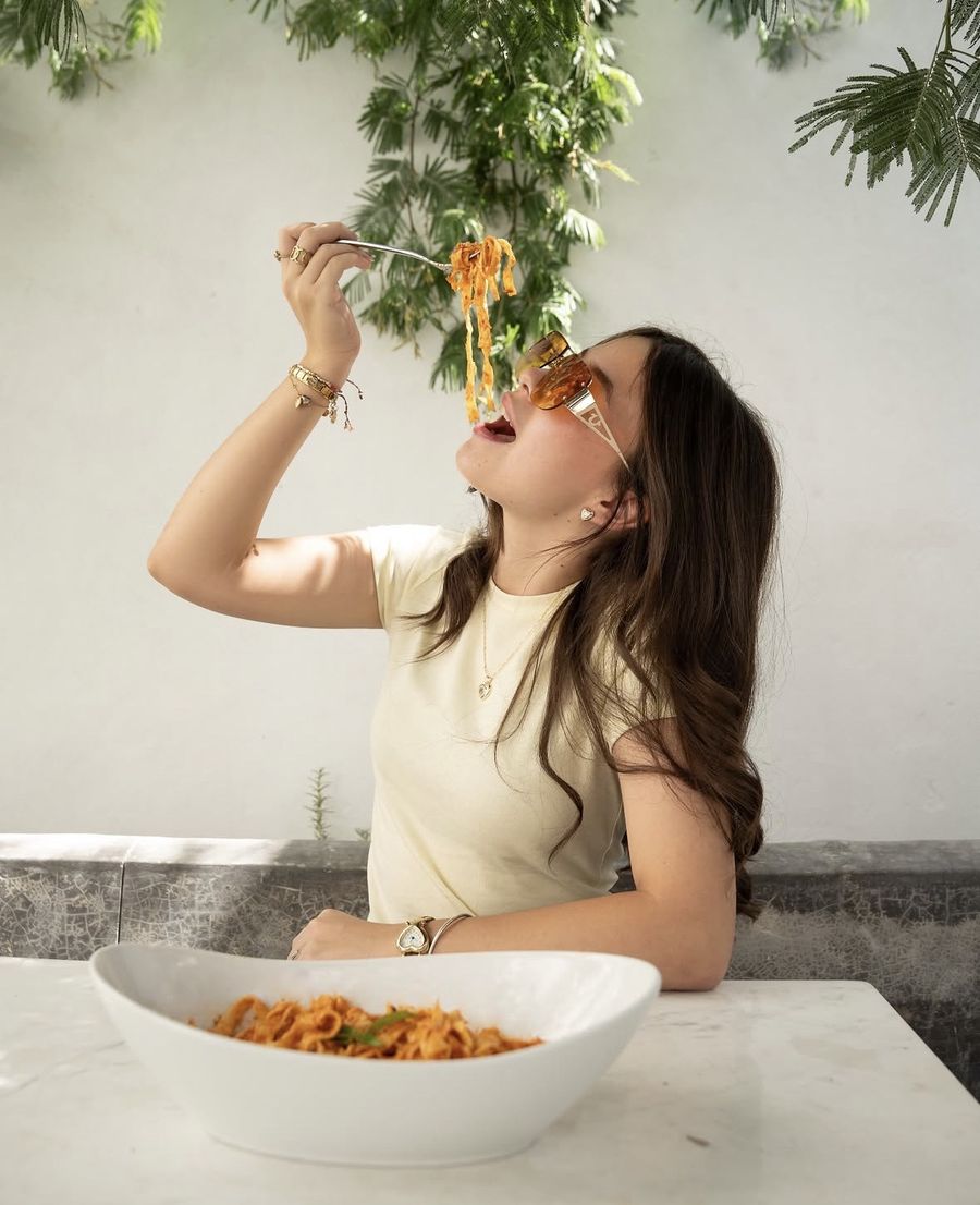 Mujer levantando pasta con el tenedor sobre un plato en la mesa