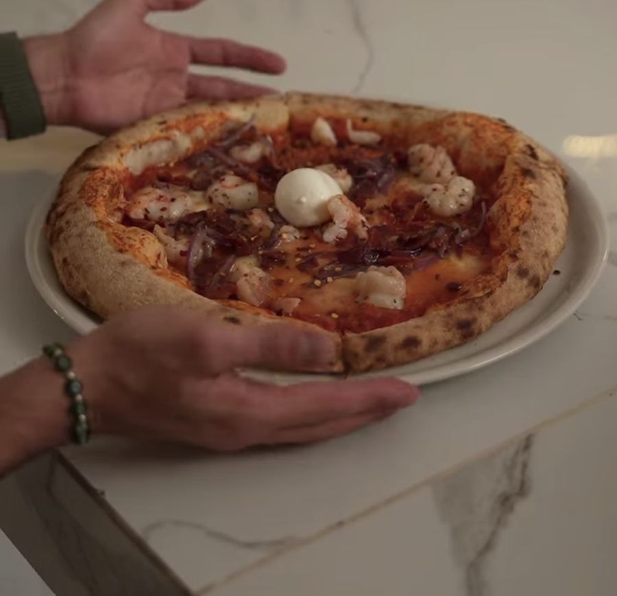 Pizza napolitana con burrata al centro, sostenida con ambas manos