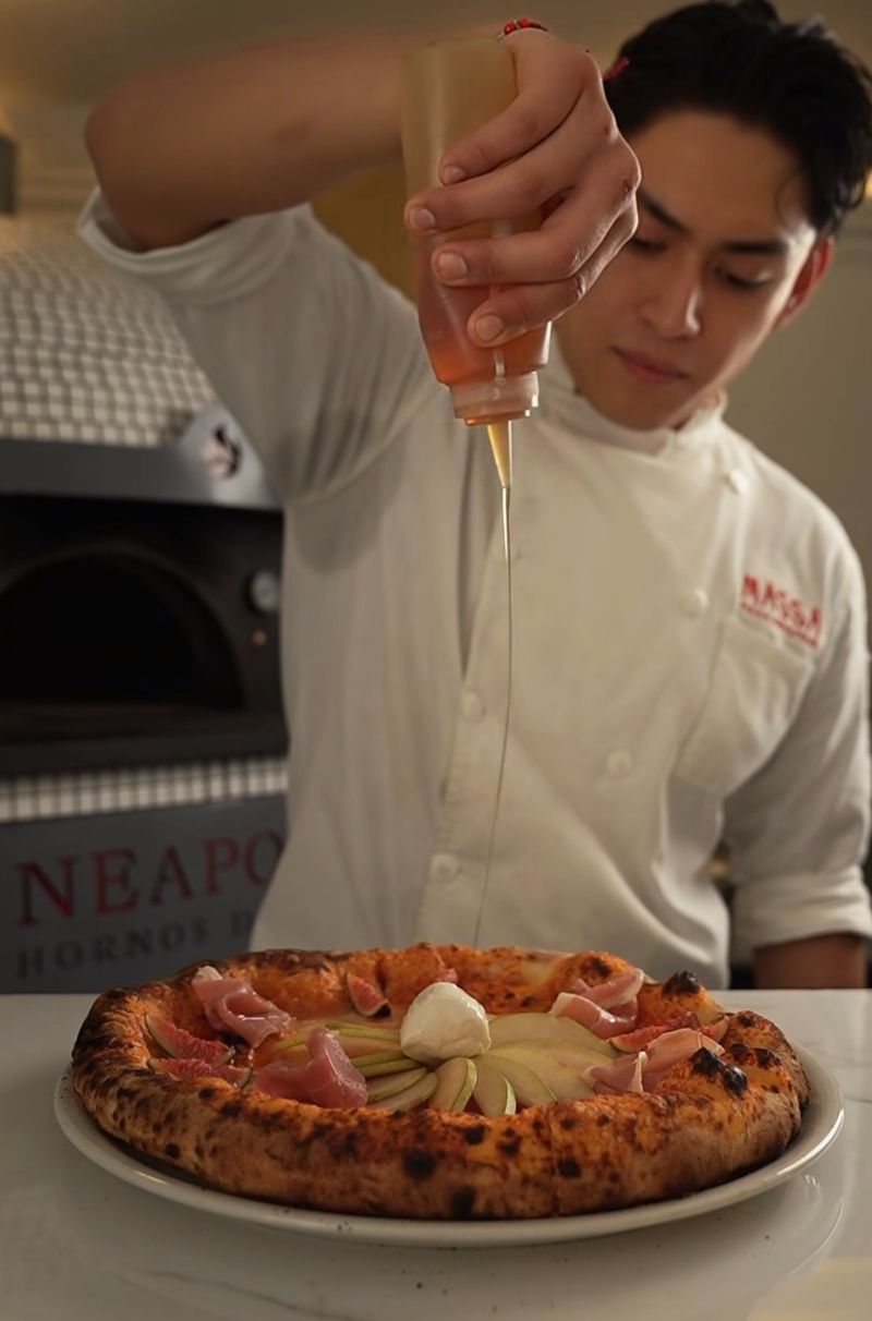 Pizzaiolo vertiendo miel sobre una pizza recién salida del horno